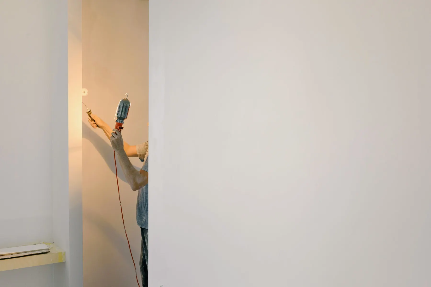 Schilder werkt met een kleine roller en een werklamp een hoek nauwkeurig af
